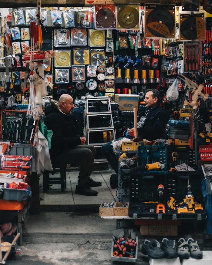 Two men in conversation at a bustling street market stall filled with tools and accessories.