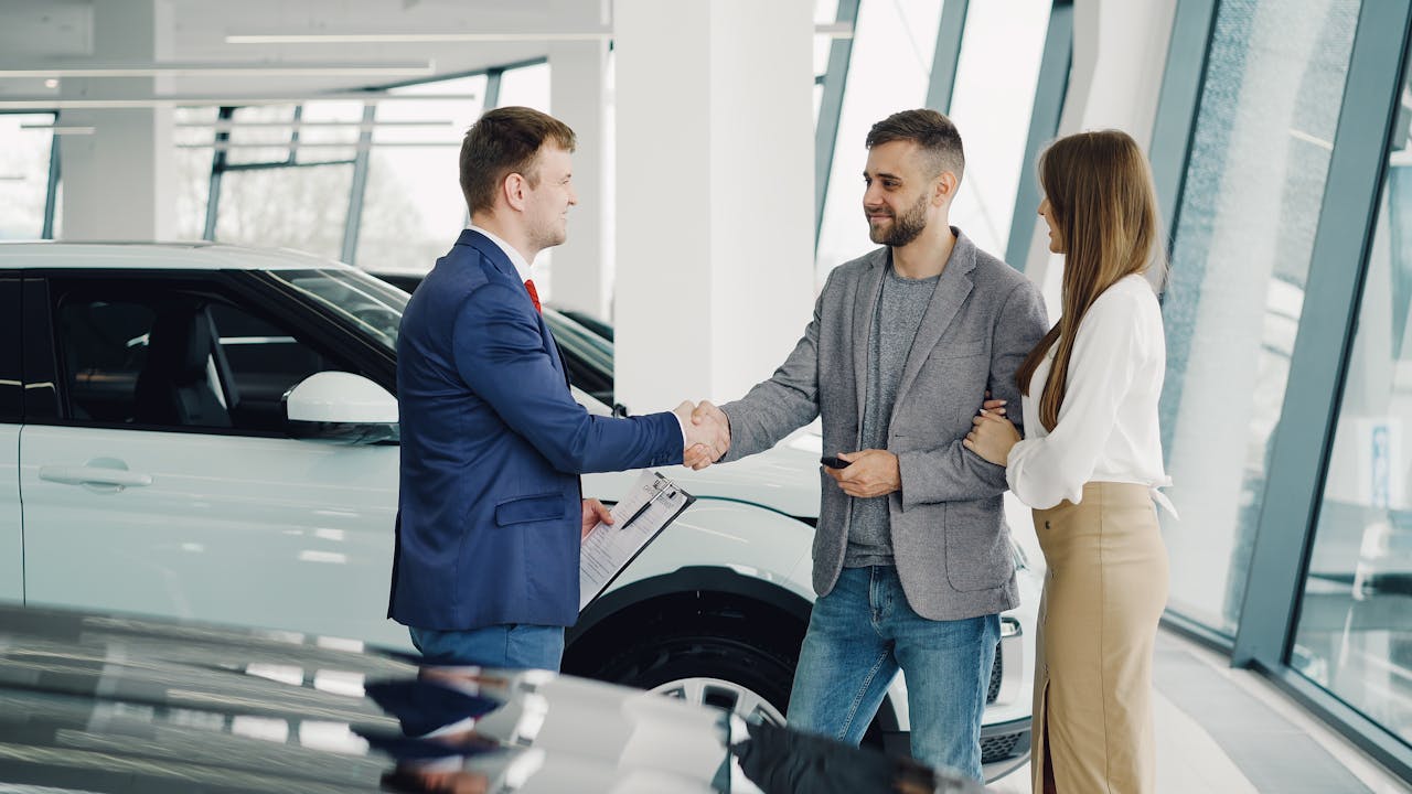 A couple completes a transaction with a salesman at a modern car dealership.